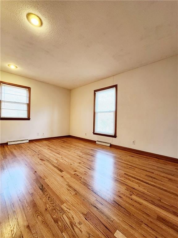 empty room with a baseboard heating unit, baseboards, light wood finished floors, and a textured ceiling