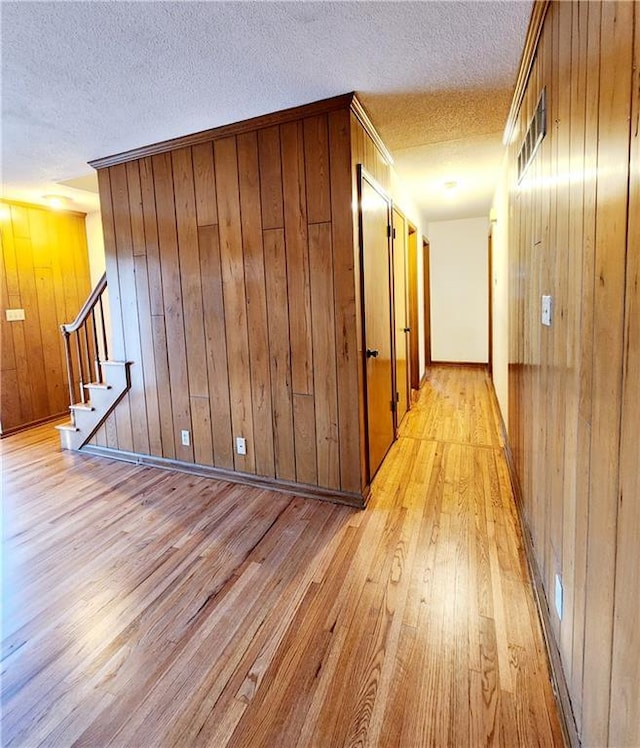 corridor with wooden walls, stairway, a textured ceiling, and light wood-style floors