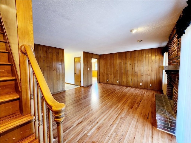 unfurnished living room with light wood-style flooring, a textured ceiling, stairway, wood walls, and a fireplace