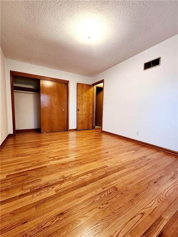 unfurnished bedroom with visible vents, baseboards, light wood-style floors, a closet, and a textured ceiling