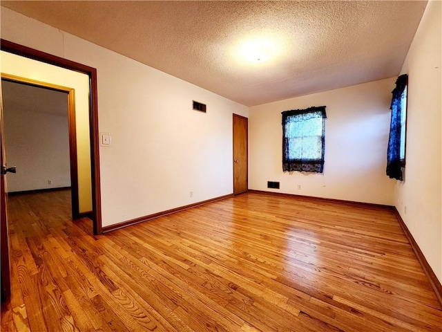 unfurnished room with baseboards, visible vents, light wood finished floors, and a textured ceiling