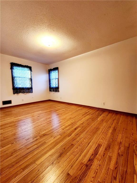 empty room with baseboards, light wood-type flooring, and a textured ceiling