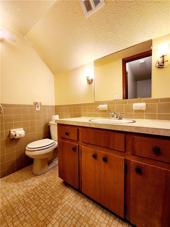 bathroom with visible vents, toilet, a textured ceiling, and lofted ceiling