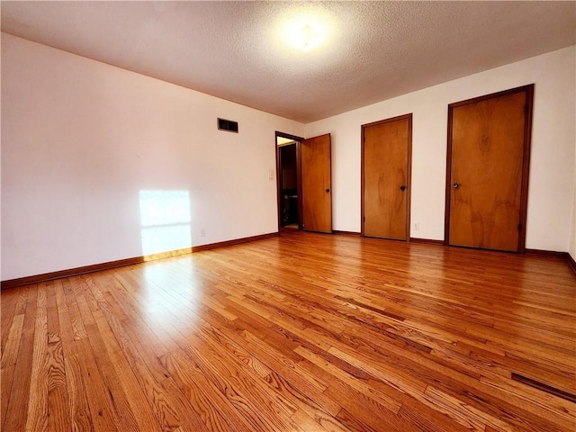 unfurnished bedroom featuring visible vents, baseboards, light wood-style flooring, multiple closets, and a textured ceiling