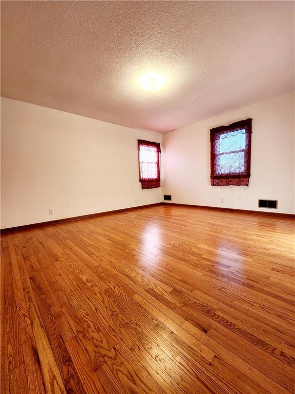 unfurnished room with visible vents, a textured ceiling, light wood-type flooring, and baseboards