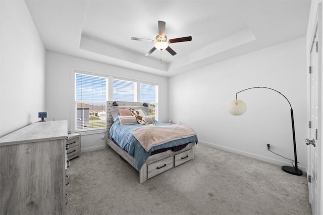 bedroom with light carpet, ceiling fan, a raised ceiling, and baseboards