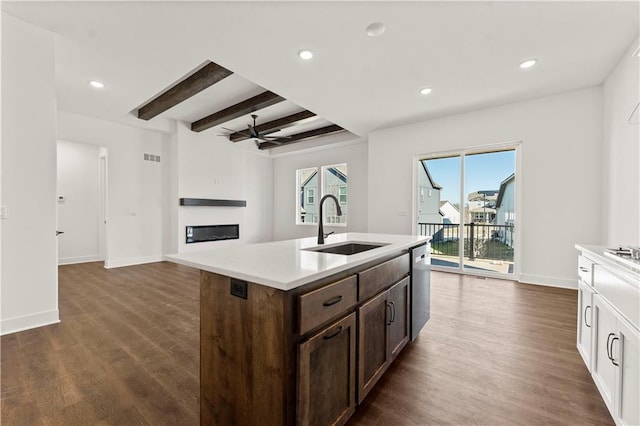 kitchen featuring a glass covered fireplace, beamed ceiling, dark wood-style flooring, light countertops, and a sink