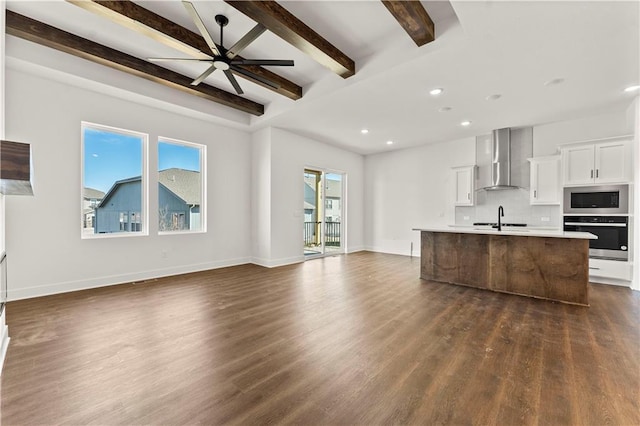 kitchen with a center island with sink, stainless steel appliances, open floor plan, a sink, and wall chimney exhaust hood