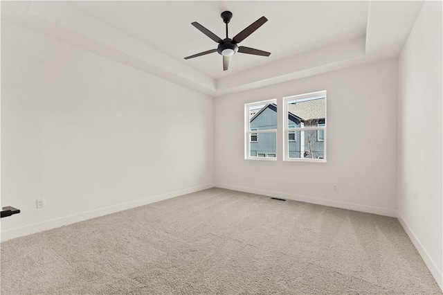 carpeted spare room featuring ceiling fan, a tray ceiling, visible vents, and baseboards