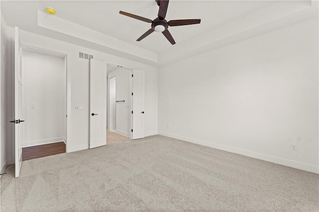 unfurnished bedroom with a tray ceiling, visible vents, carpet flooring, ceiling fan, and baseboards