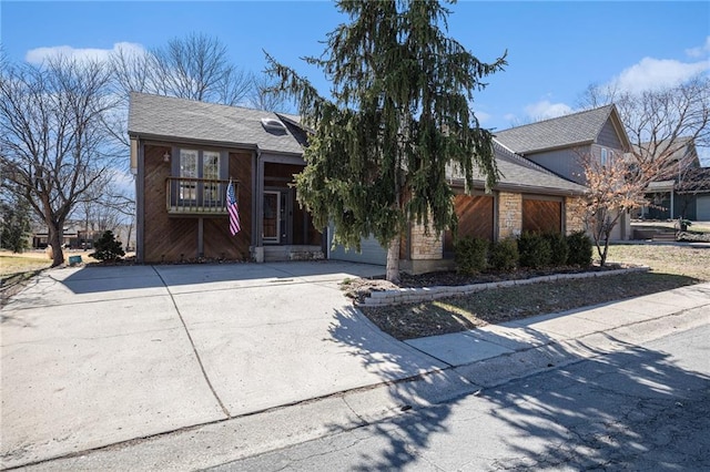 view of front of house with driveway, stone siding, a balcony, and a shingled roof