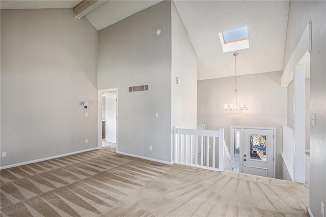 empty room with a skylight, visible vents, a notable chandelier, carpet floors, and beam ceiling