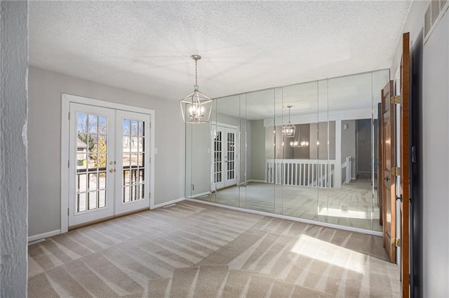 unfurnished dining area with a textured ceiling, french doors, carpet flooring, and a notable chandelier