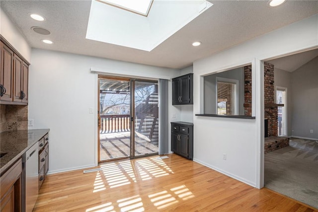 kitchen with a skylight, tasteful backsplash, light wood finished floors, baseboards, and dishwasher