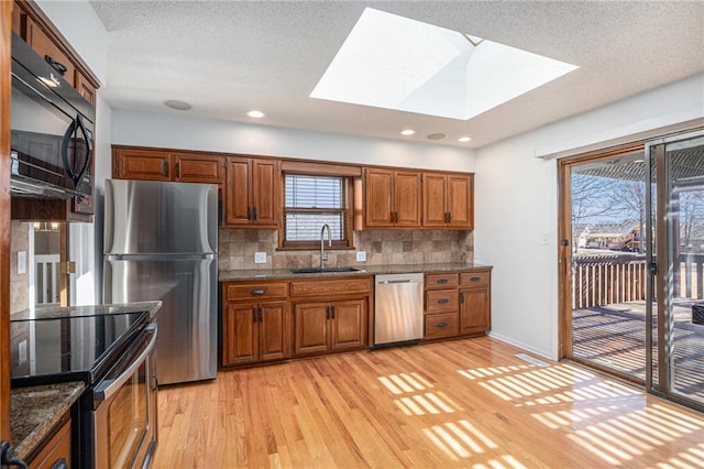 kitchen with stainless steel appliances, decorative backsplash, light wood-style floors, brown cabinetry, and a sink