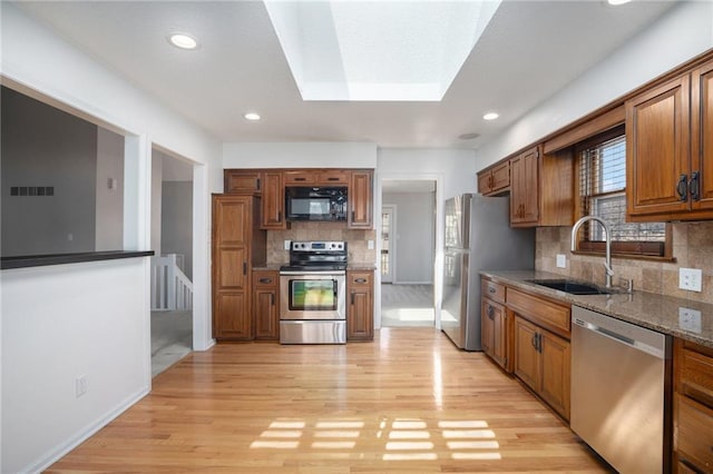 kitchen with light wood-style flooring, appliances with stainless steel finishes, brown cabinetry, and a sink