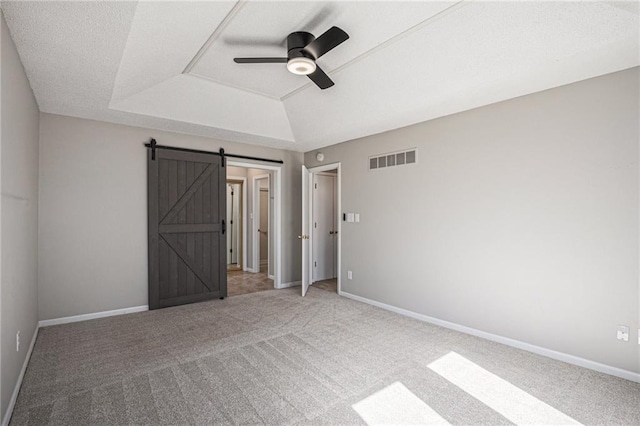 unfurnished bedroom with a barn door, baseboards, visible vents, a tray ceiling, and carpet floors