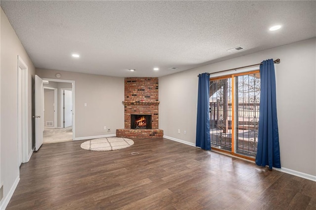 unfurnished living room with a brick fireplace, visible vents, a textured ceiling, and wood finished floors