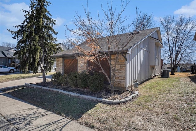 view of property exterior featuring cooling unit, stone siding, a yard, roof with shingles, and driveway