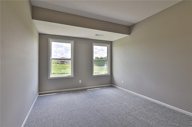 empty room featuring a textured ceiling, carpet, visible vents, and baseboards