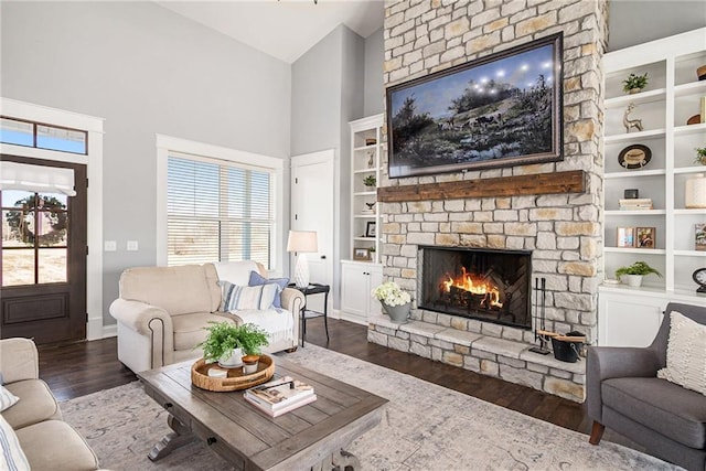 living area with high vaulted ceiling, built in features, wood finished floors, a stone fireplace, and baseboards