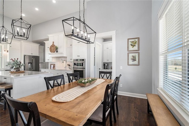 dining room with baseboards, a notable chandelier, a towering ceiling, and dark wood finished floors