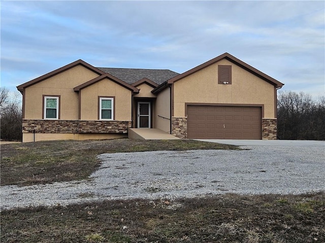 view of front facade with gravel driveway, stone siding, an attached garage, and stucco siding