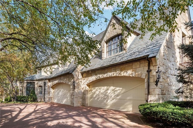 view of front of property featuring a high end roof, stone siding, driveway, and an attached garage