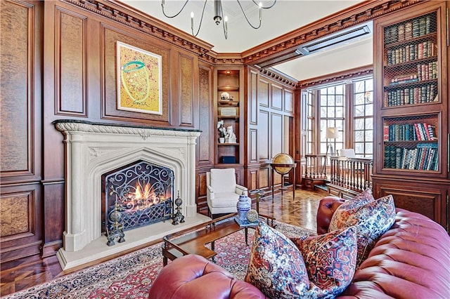 living area featuring built in shelves, wood finished floors, a chandelier, and a premium fireplace