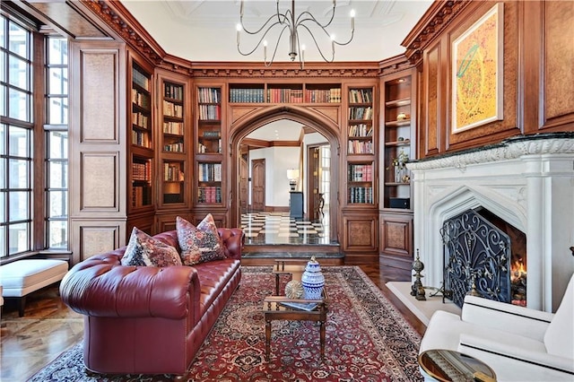 living area featuring arched walkways, a warm lit fireplace, a chandelier, built in features, and crown molding