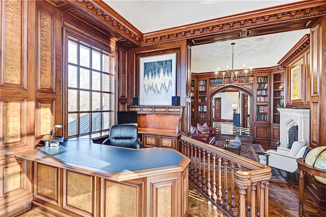 office space with built in features, arched walkways, ornamental molding, an inviting chandelier, and a fireplace