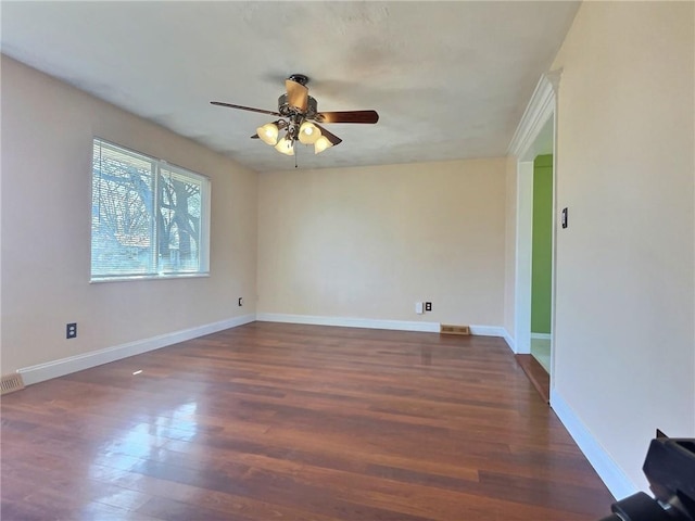 empty room featuring dark wood-style floors, visible vents, a ceiling fan, and baseboards