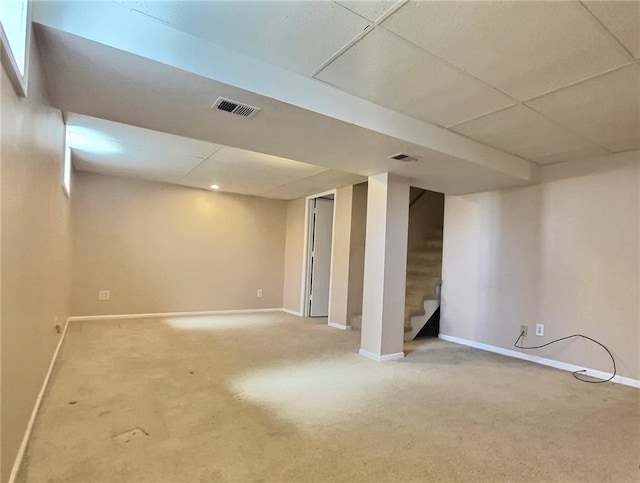 finished below grade area featuring visible vents, a drop ceiling, stairway, carpet flooring, and baseboards