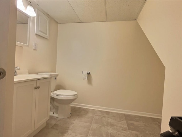 bathroom featuring vanity, toilet, baseboards, and a drop ceiling