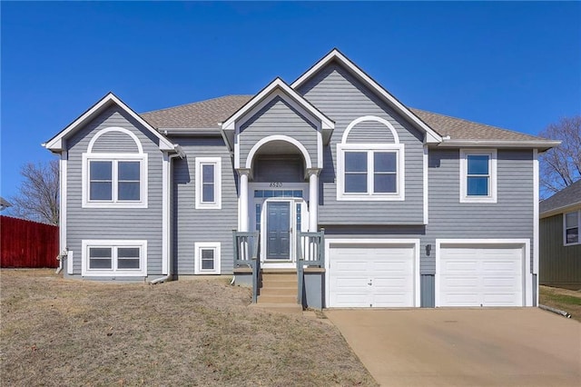 raised ranch featuring concrete driveway, roof with shingles, an attached garage, and fence