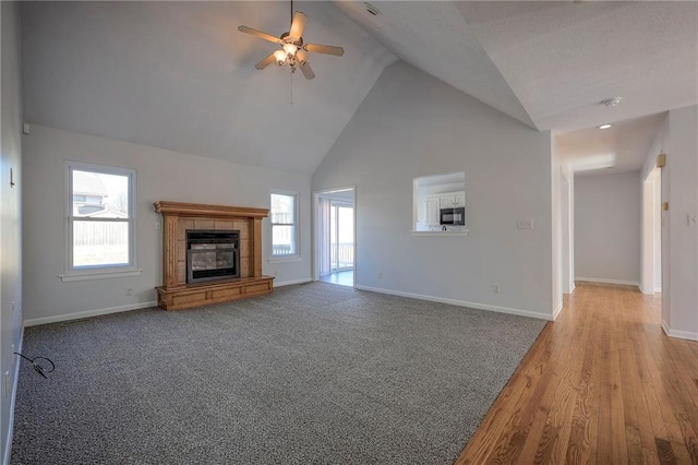 unfurnished living room with baseboards, high vaulted ceiling, ceiling fan, and a tile fireplace