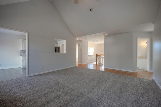 spare room with high vaulted ceiling, wood finished floors, carpet flooring, and baseboards