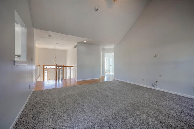 carpeted empty room featuring high vaulted ceiling, visible vents, and baseboards