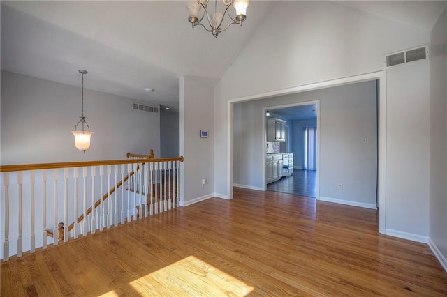 spare room featuring high vaulted ceiling, wood finished floors, visible vents, and an inviting chandelier