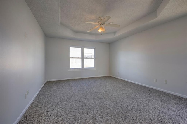 carpeted empty room featuring a textured ceiling, a tray ceiling, a ceiling fan, and baseboards