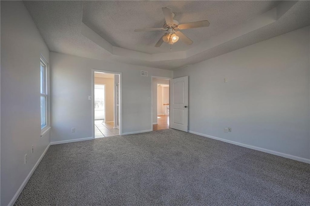 unfurnished bedroom with a tray ceiling, carpet flooring, a textured ceiling, and baseboards