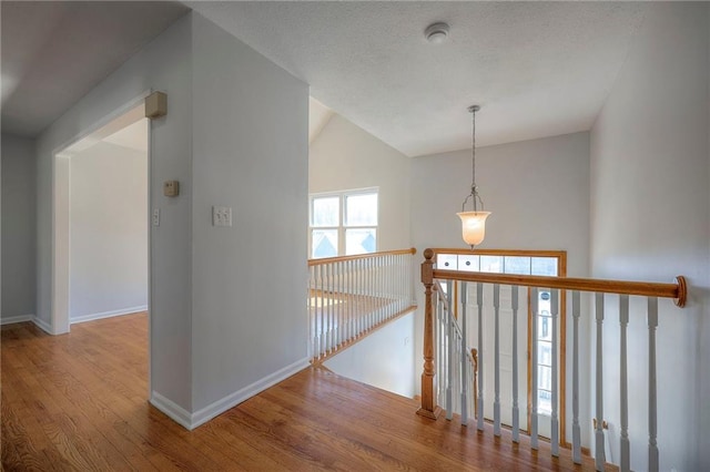 hallway with an upstairs landing, a textured ceiling, baseboards, and wood finished floors