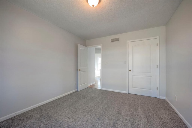 unfurnished bedroom featuring carpet, visible vents, a textured ceiling, and baseboards