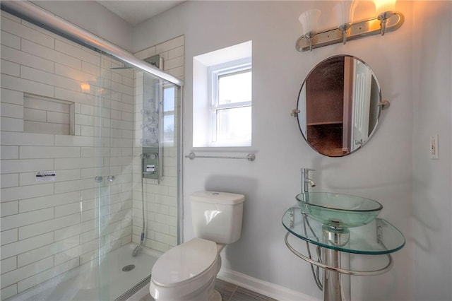 bathroom with toilet, a shower stall, baseboards, and a sink