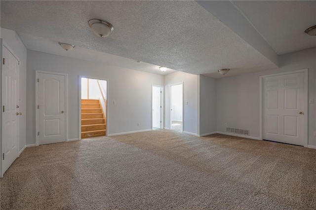 unfurnished room featuring a textured ceiling, carpet floors, visible vents, baseboards, and stairway