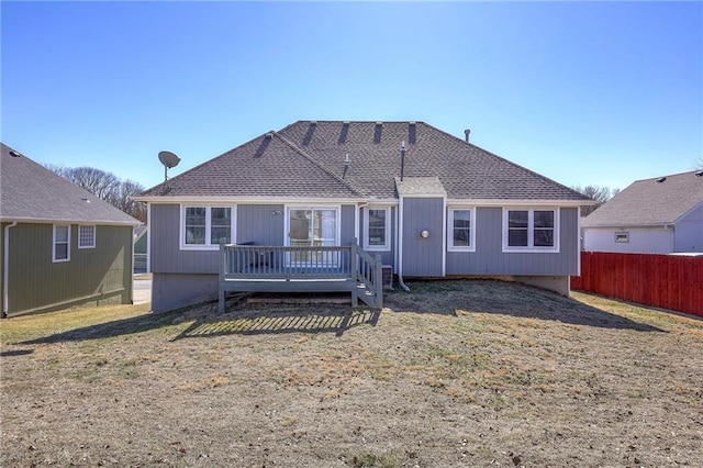 rear view of house featuring a deck, a yard, a shingled roof, and fence