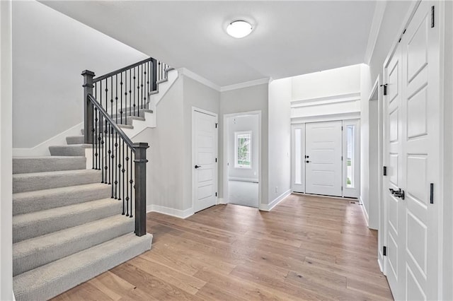 foyer featuring ornamental molding, light wood-type flooring, stairway, and baseboards