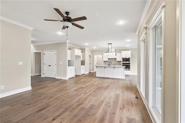 unfurnished living room with baseboards, light wood-style flooring, ceiling fan, crown molding, and a sink