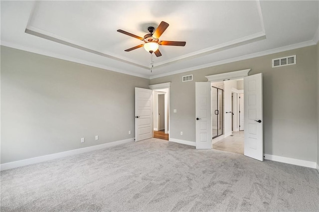 unfurnished bedroom with light carpet, a tray ceiling, visible vents, and baseboards