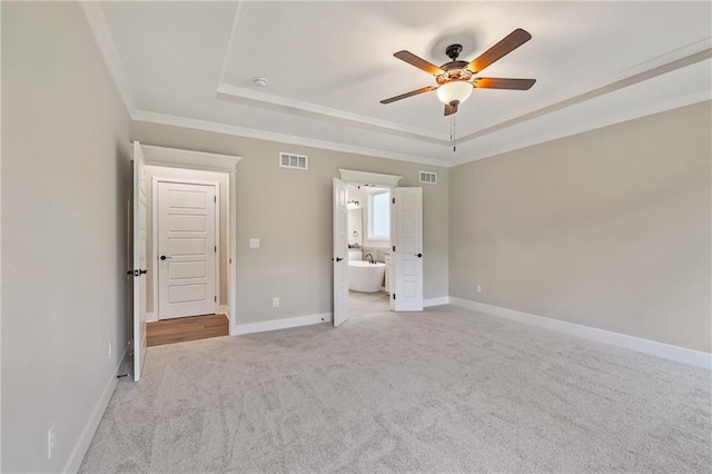 unfurnished bedroom featuring visible vents, a tray ceiling, baseboards, and light colored carpet